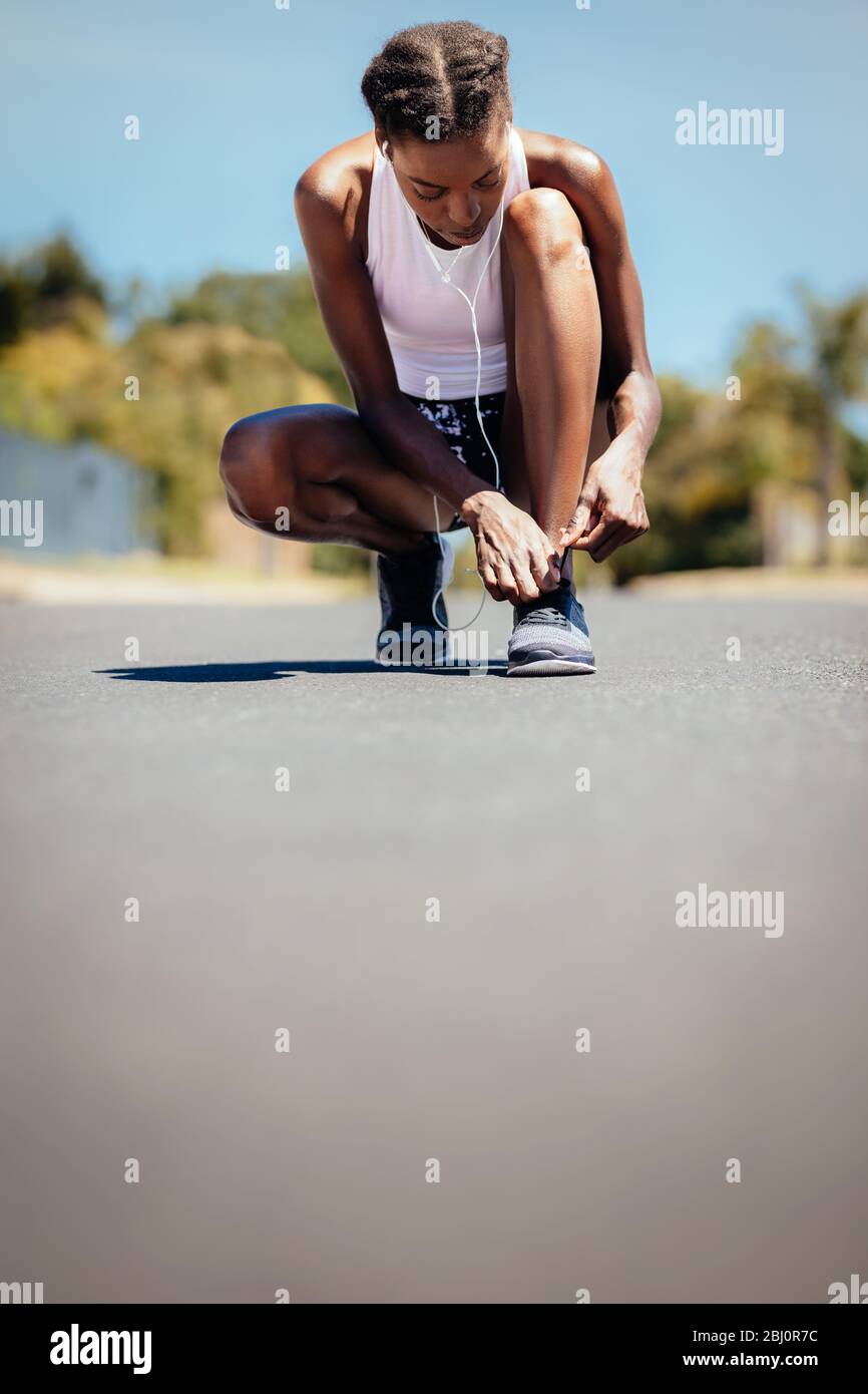 Fitness woman tying her shoelace on the road outdoors. Female on morning run fastening her shoe laces. Stock Photo