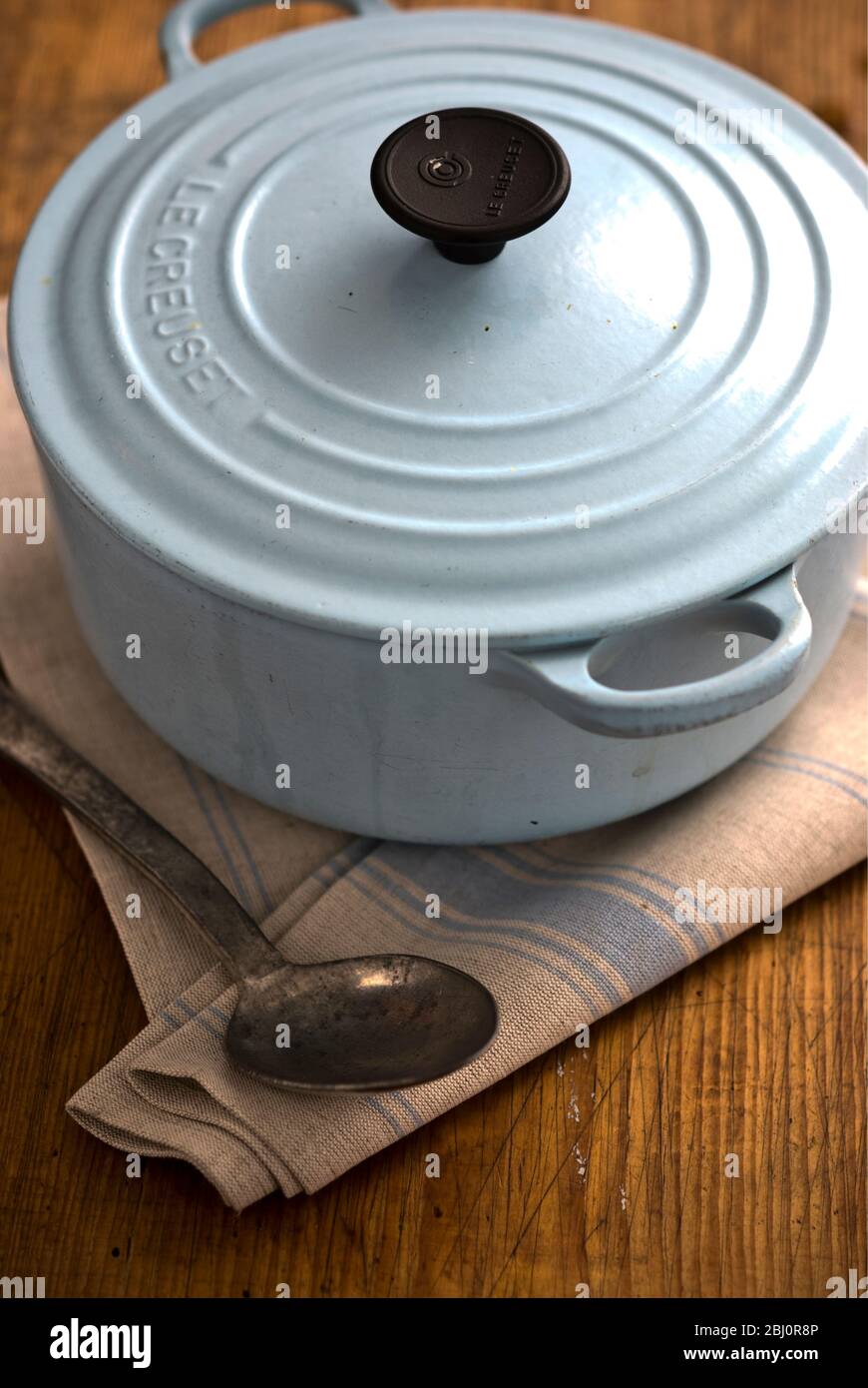 Blue enamel Le Creuset casserole on wooden work surface - Stock Photo
