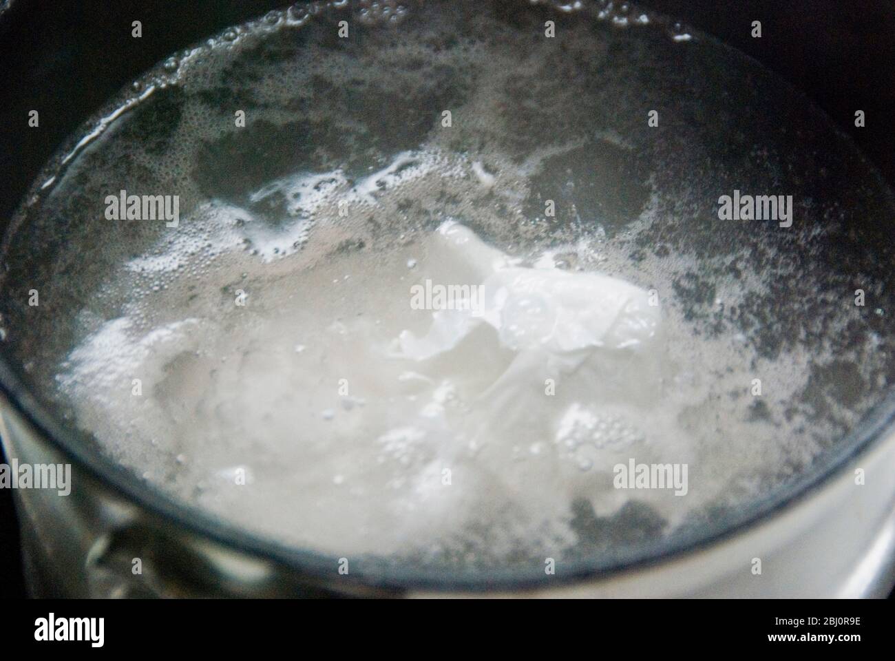 Detail of pan of water simmering with a poached egg - Stock Photo