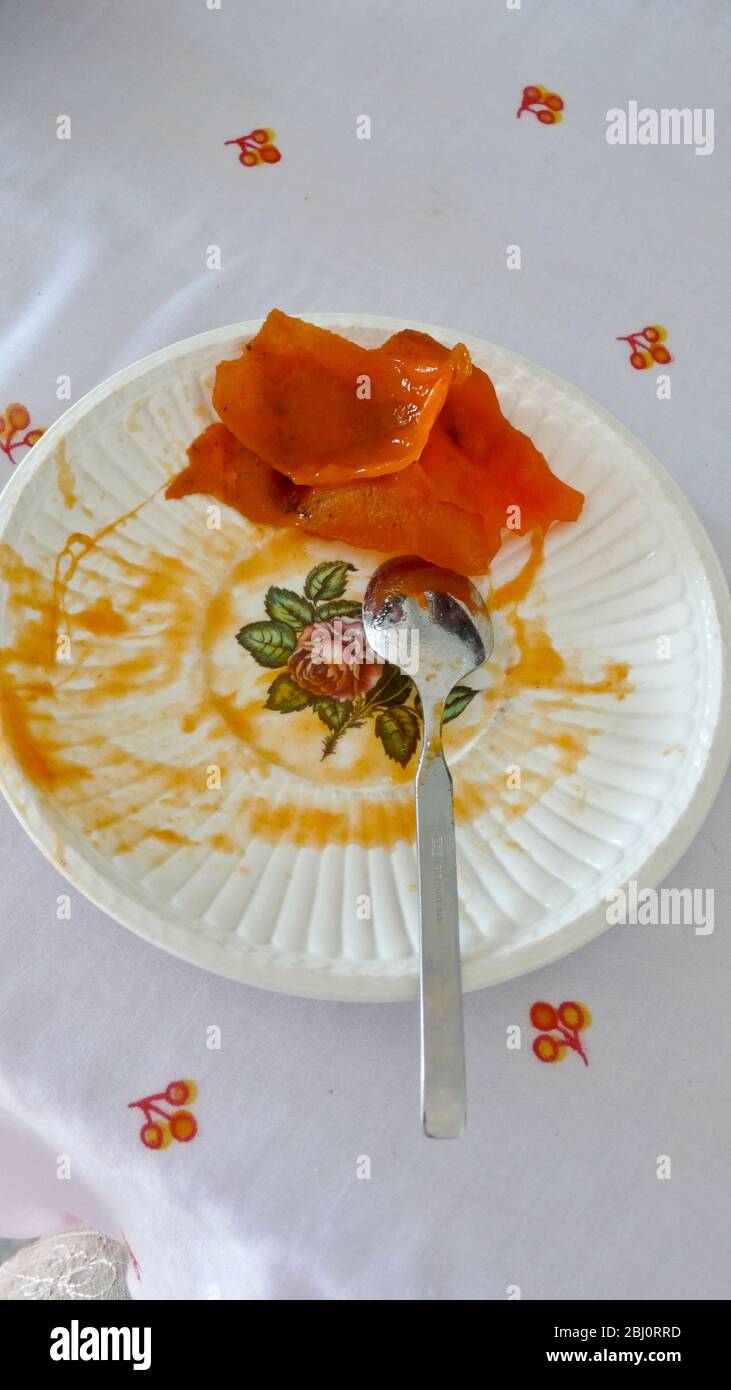 Ripe persimmon fruit on decorated saucer with teaspoon, having been eaten! - Stock Photo