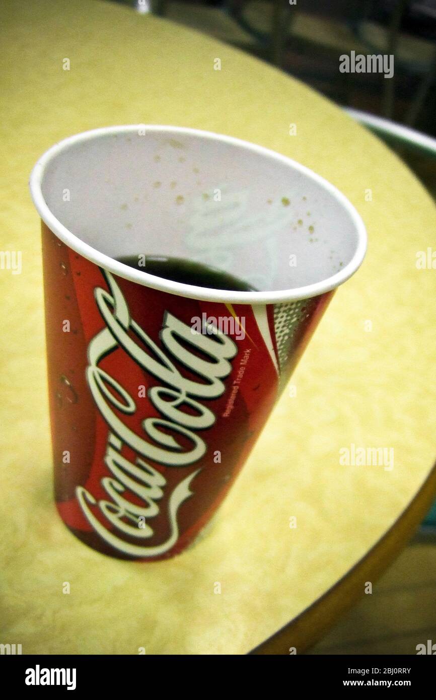 Paper cup of Coca-Cola on yellow table in motorway services restaurant - Stock Photo