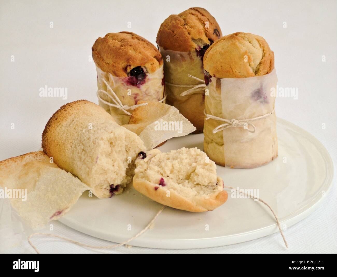 Blueberry muffins made in talll paper cases of greaseproof paper tied with string - Stock Photo