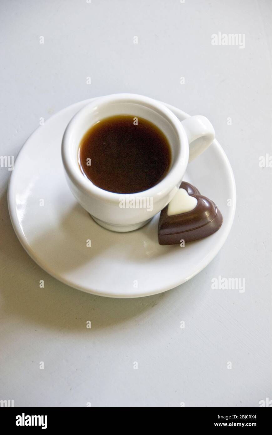 Heart shaped chocolate on saucer of small espresso cup of black coffee - Stock Photo