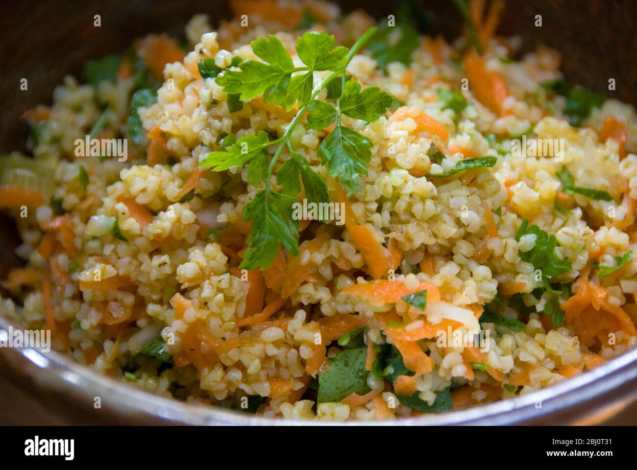 Healthy lunchtime salad of burghul wheat with grated carrot, lemon juice, olive oil, chopped cucumber and parsley. - Stock Photo