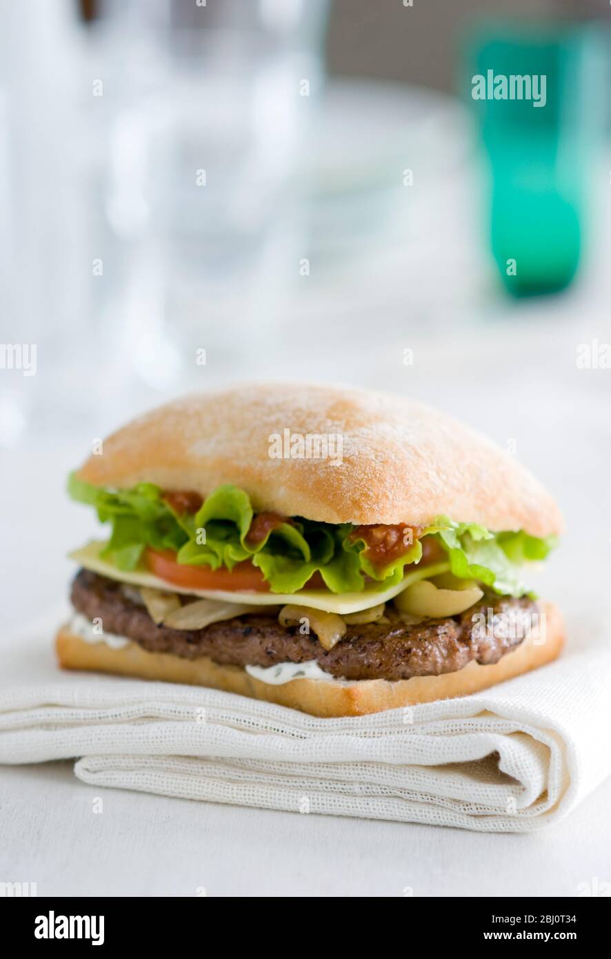 Gournet cheeseburger with salad and tomato on ciabatta bread roll on white napkin - Stock Photo