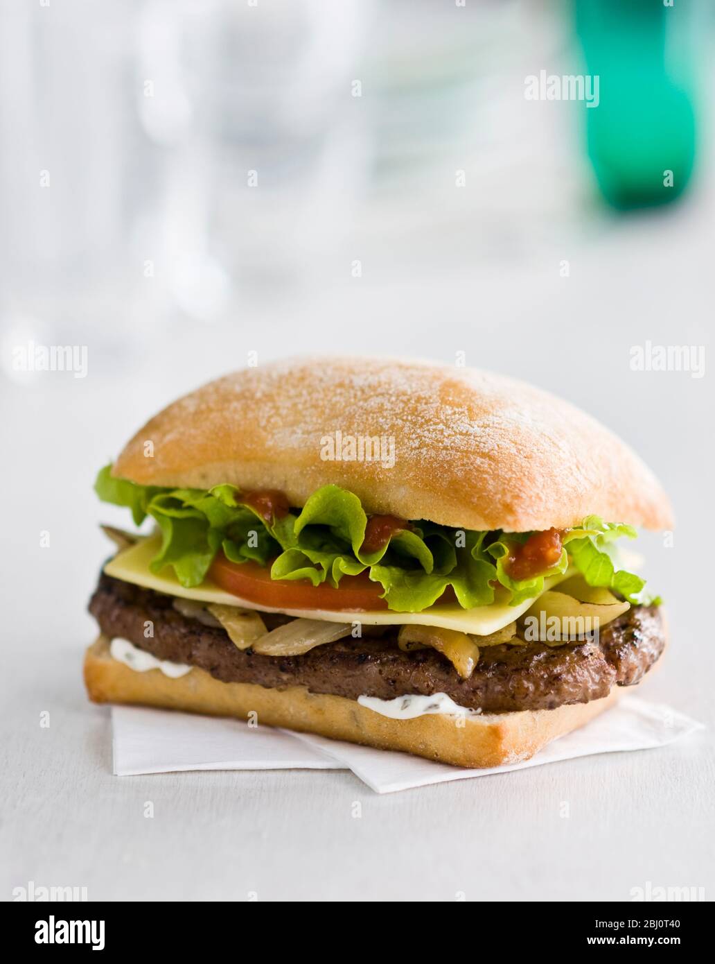 Gournet cheeseburger with salad and tomato on ciabatta bread roll on white paper napkin - Stock Photo