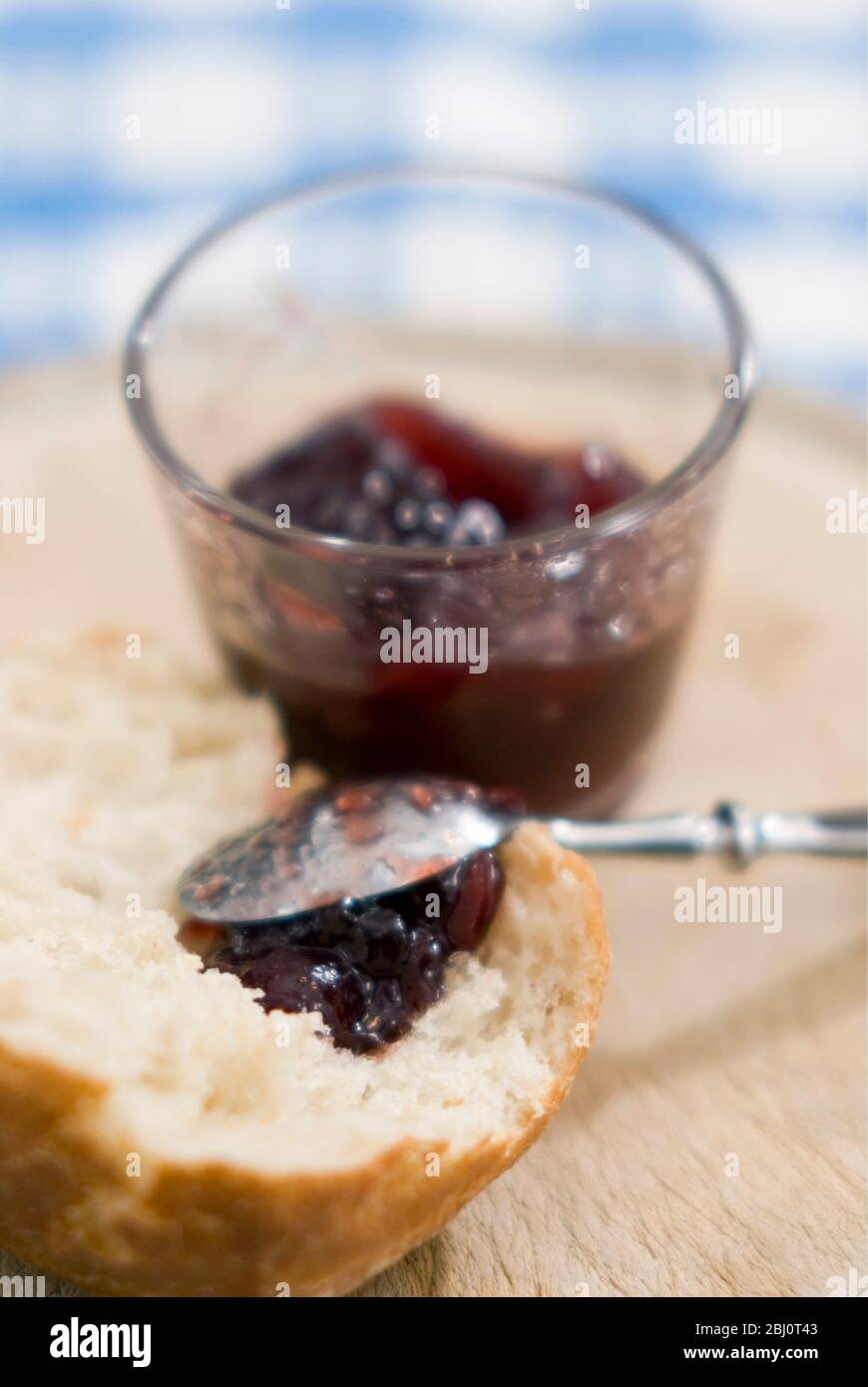 Broken crusty bread with dollop of seedless raspberry jam - Stock Photo