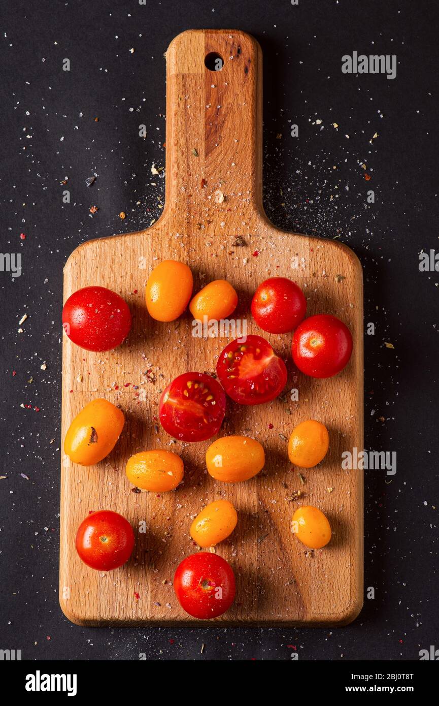 Different tomatoes cultivars on a wooden board on the black background. Multicolor tomatoes Stock Photo