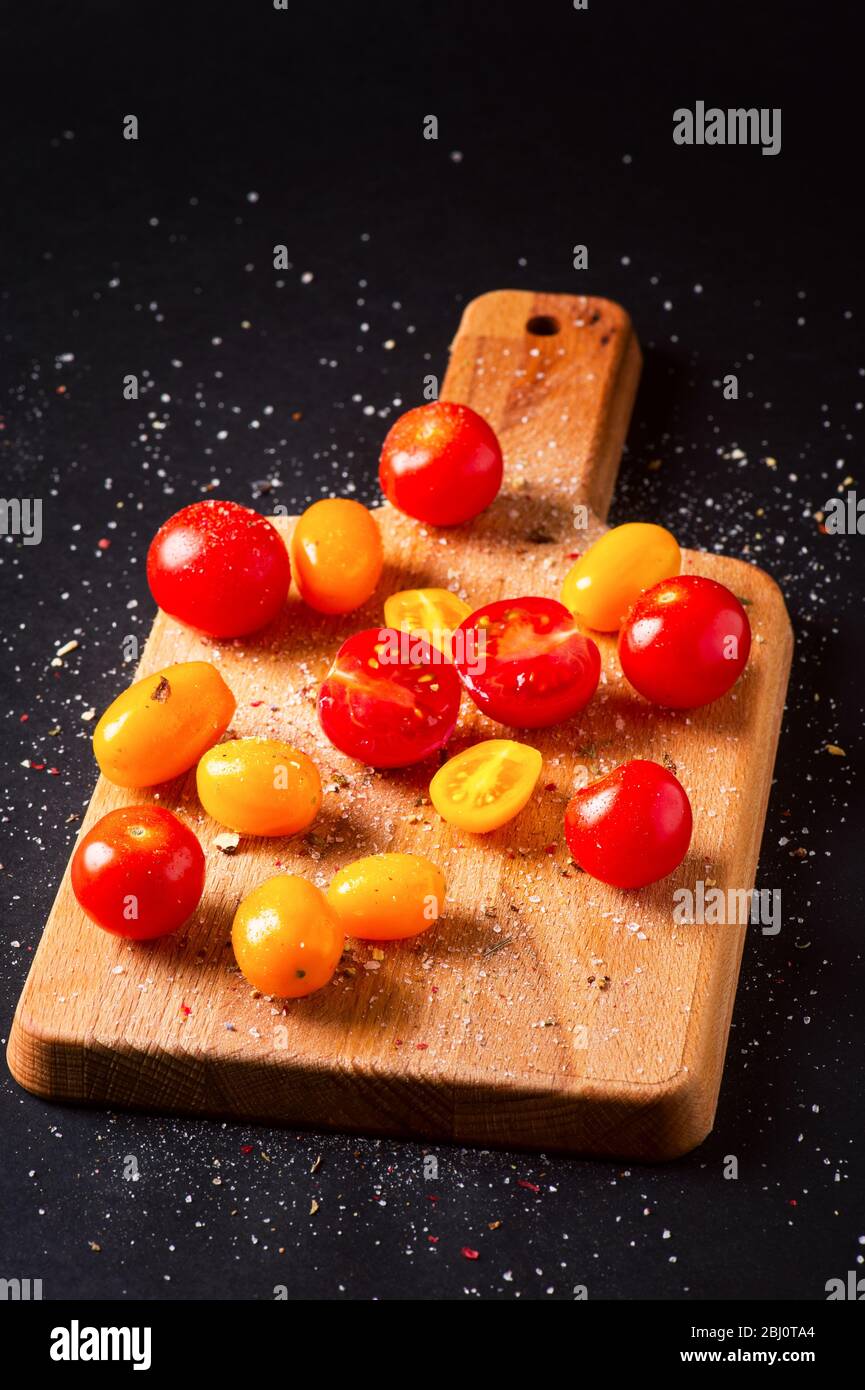 Different tomatoes cultivars on a wooden board on the black background. Multicolor tomatoes Stock Photo
