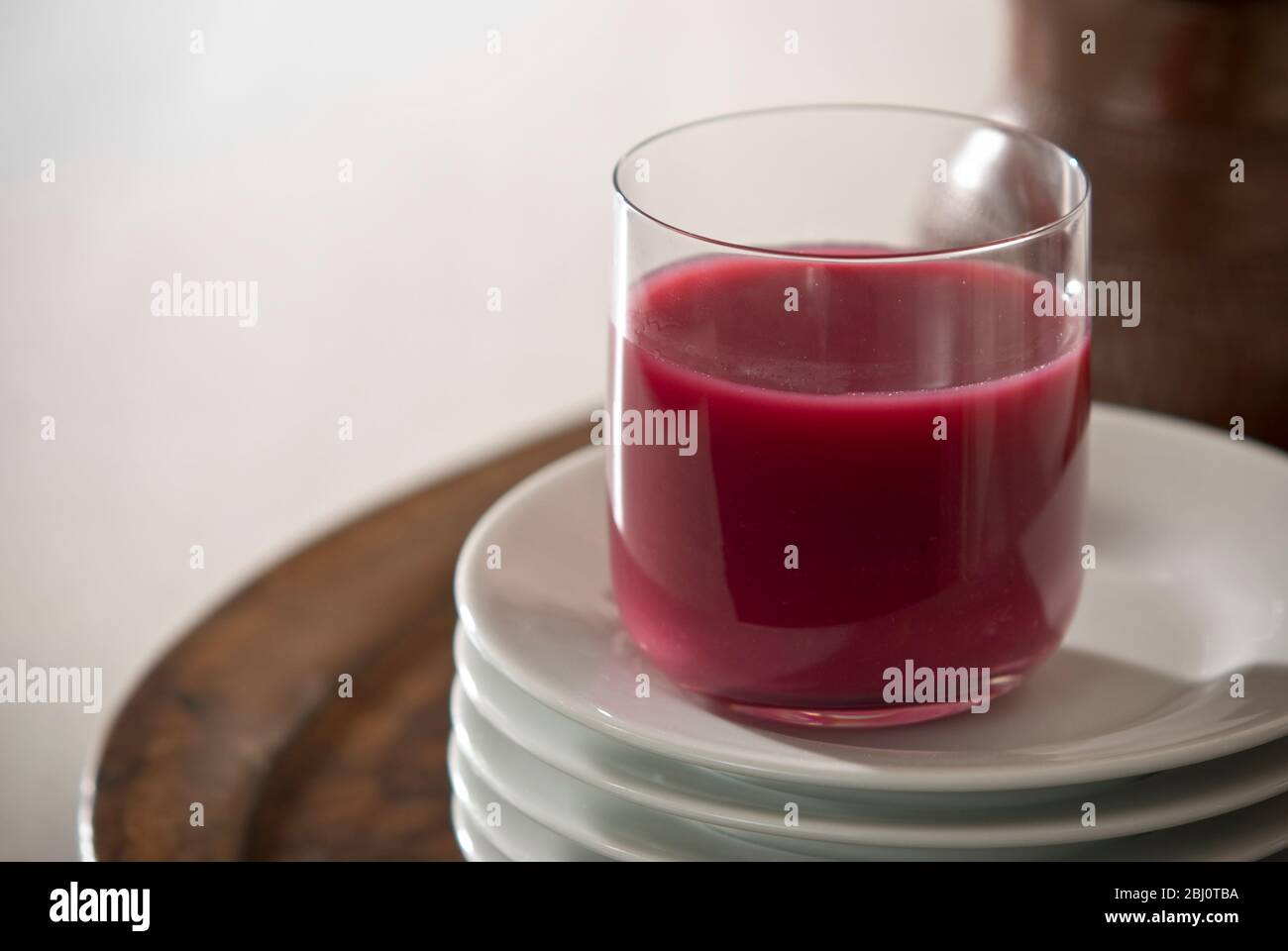 Pomegranate juice in clear glass on stack of white plates - Stock Photo