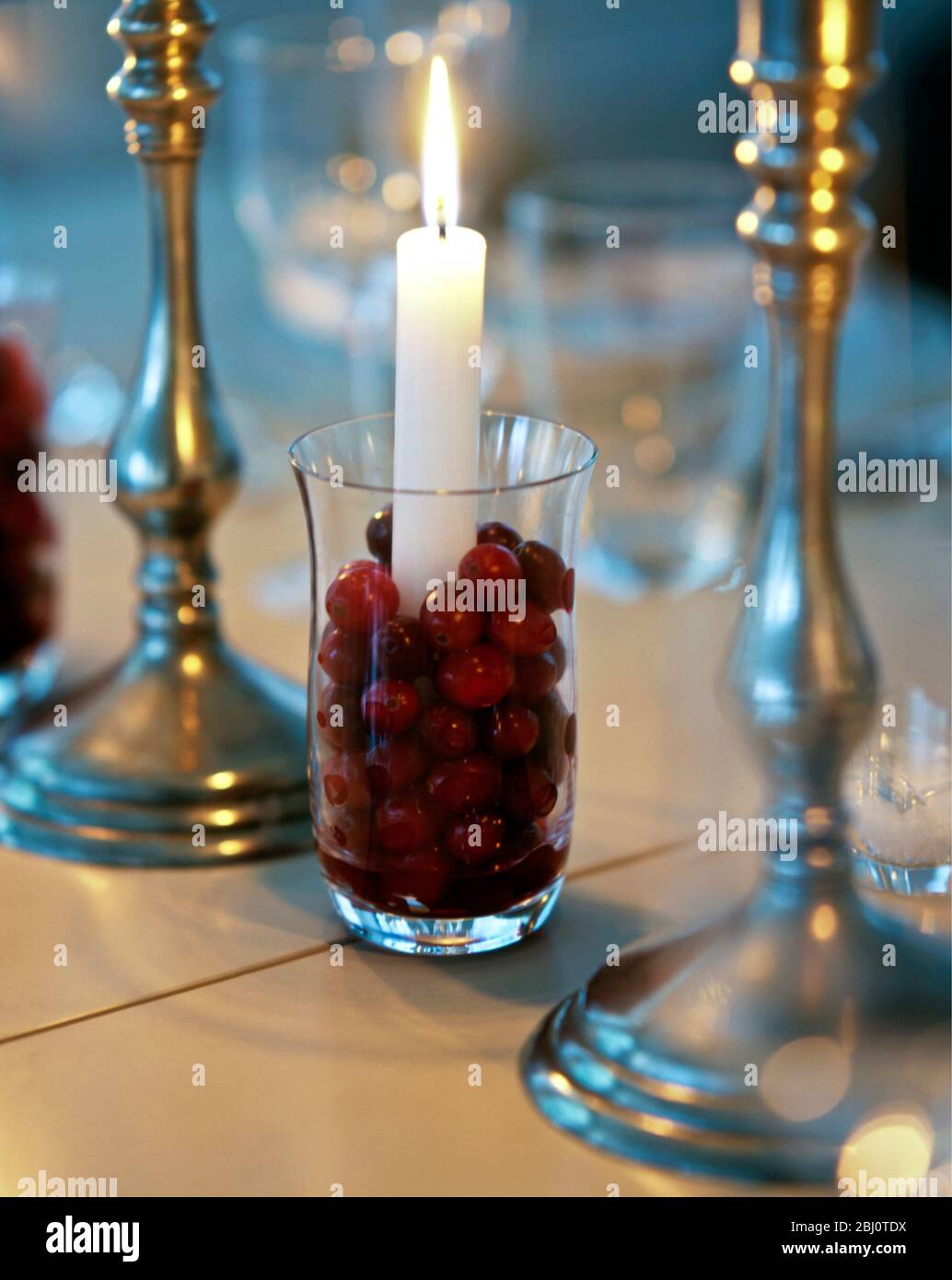 Christmas table decoration of cranberries around candle in glass with pewter candlesticks - Stock Photo
