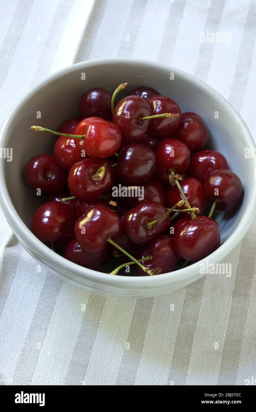 Bowl of cherries in grey pottery bowl on striped linen cloth - Stock Photo