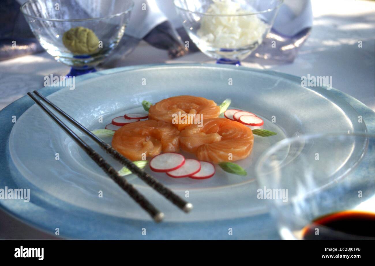 Salmon sushi beautifully arranged on white frosted glass plate, in formal table setting at outdoor summer lunch party, with wasabi, grated white radis Stock Photo
