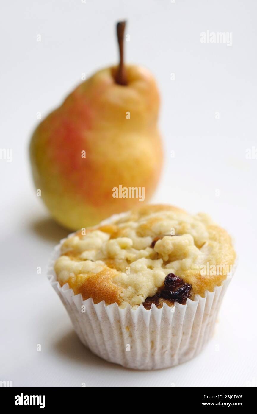 Raisin muffin in plain paper case, topped with grated pear and with whole pear behind. On white background. - Stock Photo