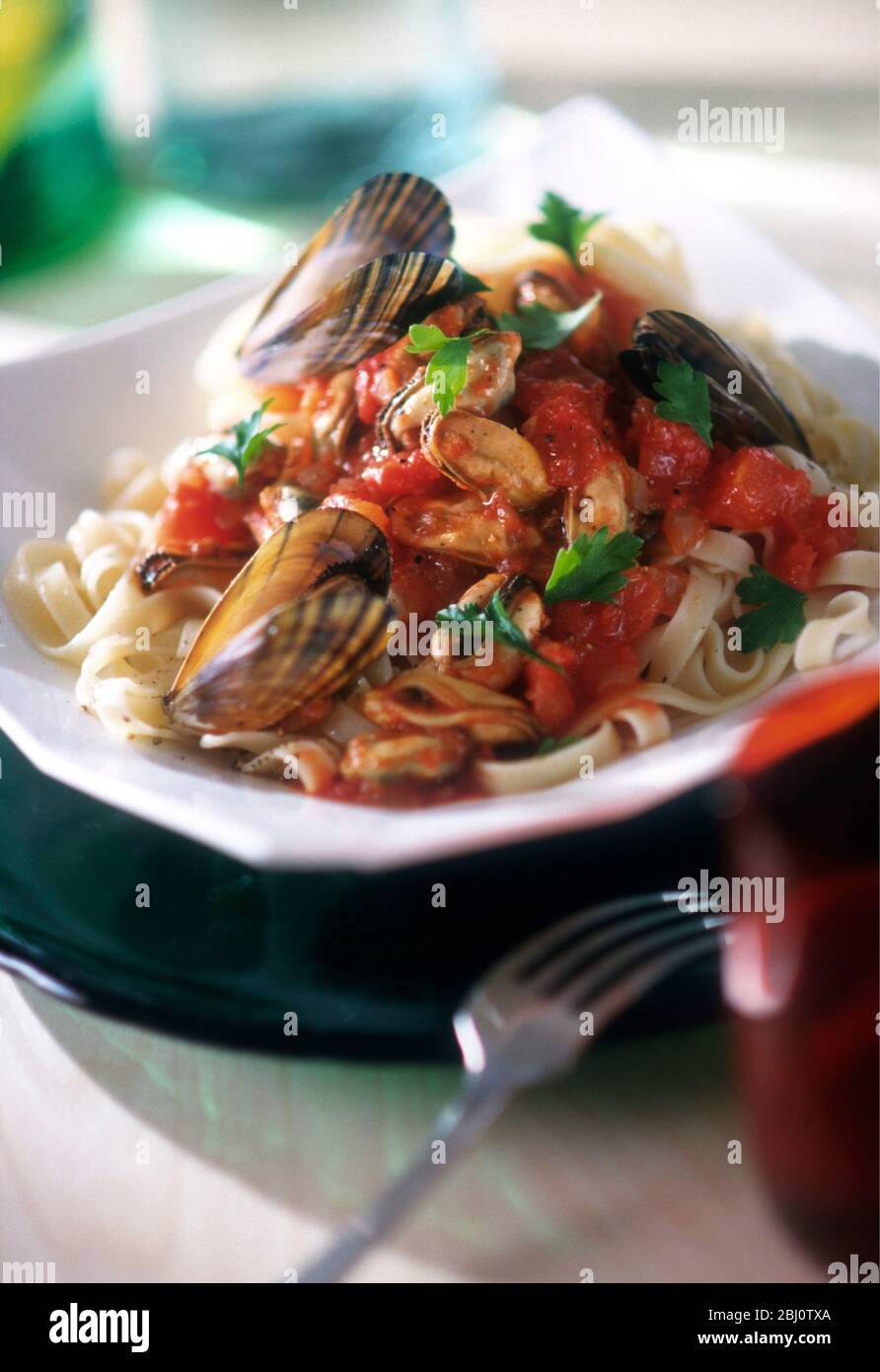 Tagliatelle noodles with sauce of mussels and tomatoes with flat parsley - Stock Photo