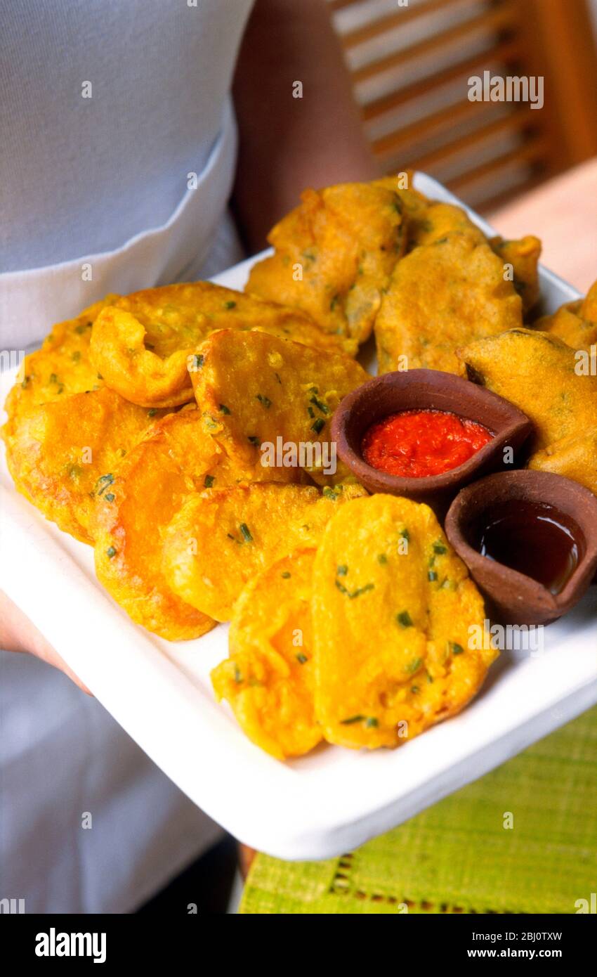 Yellow vegetarian fritters, with spicy dips, served on white platter. - Stock Photo