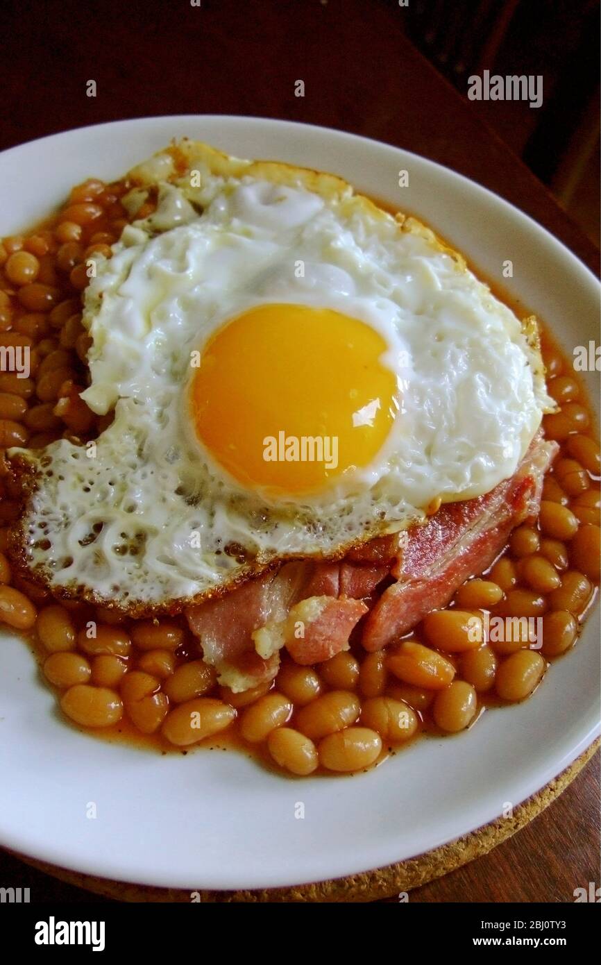 Fried egg on baked beans with streaky bacon - Stock Photo