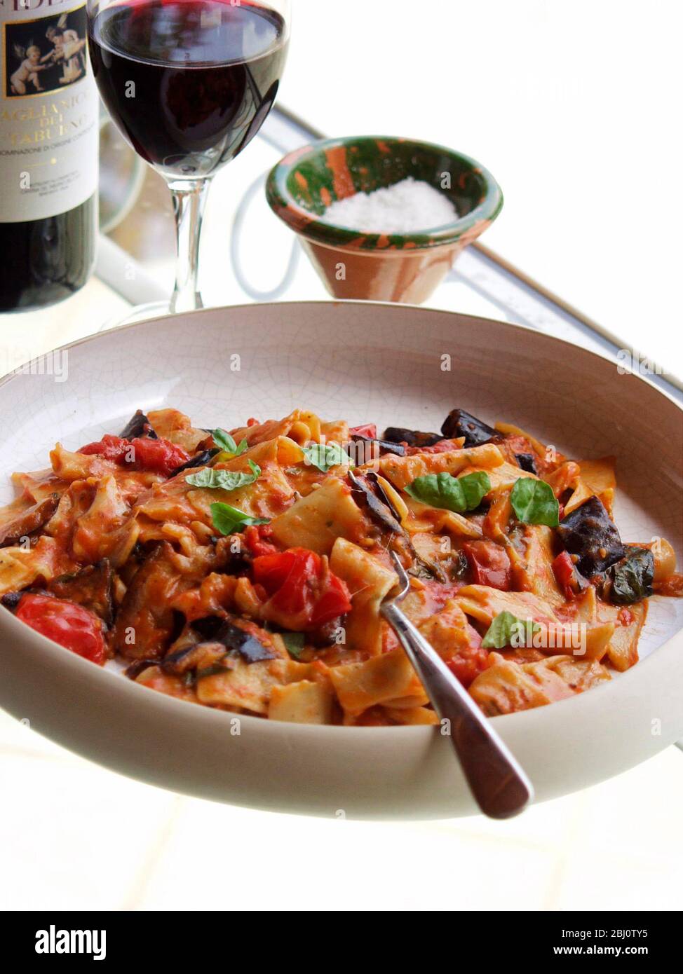 Dish of aubergine and mozzarella with pasta with wine on glass table - Stock Photo