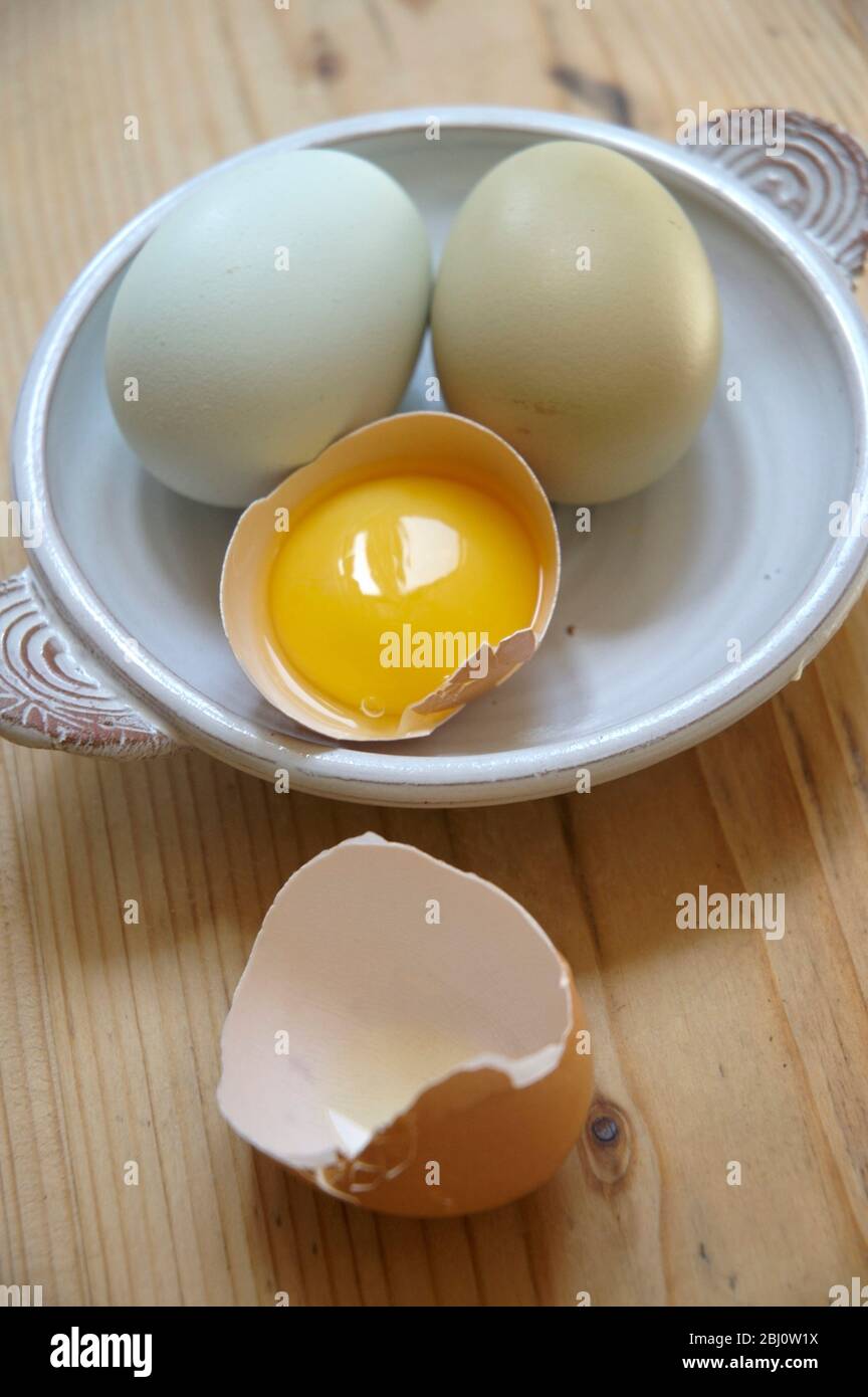 Two whole eggs and one half egg with yolk on a small ceramic dish - Stock Photo