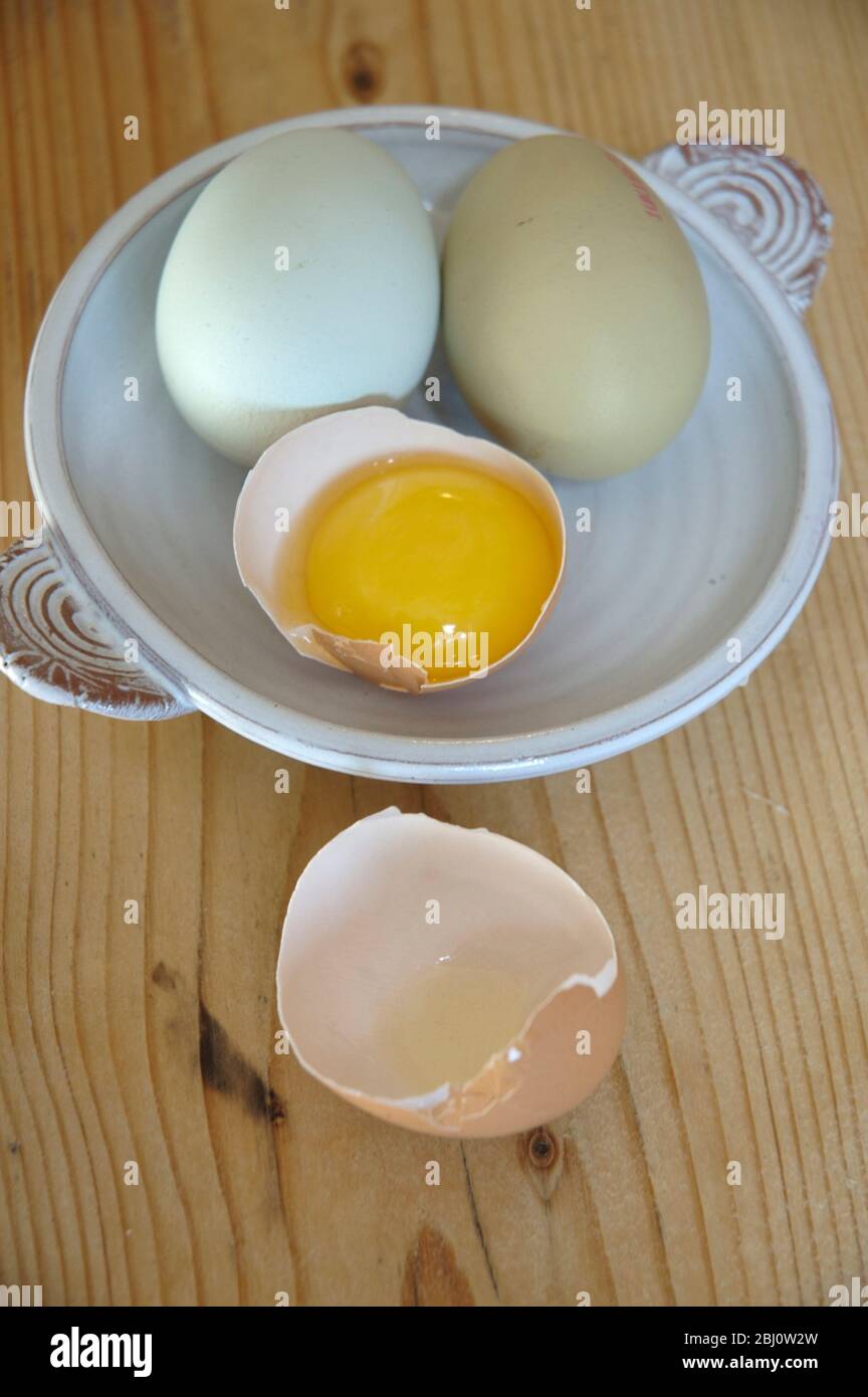 Two whole eggs and one half egg with yolk on a small ceramic dish - Stock Photo