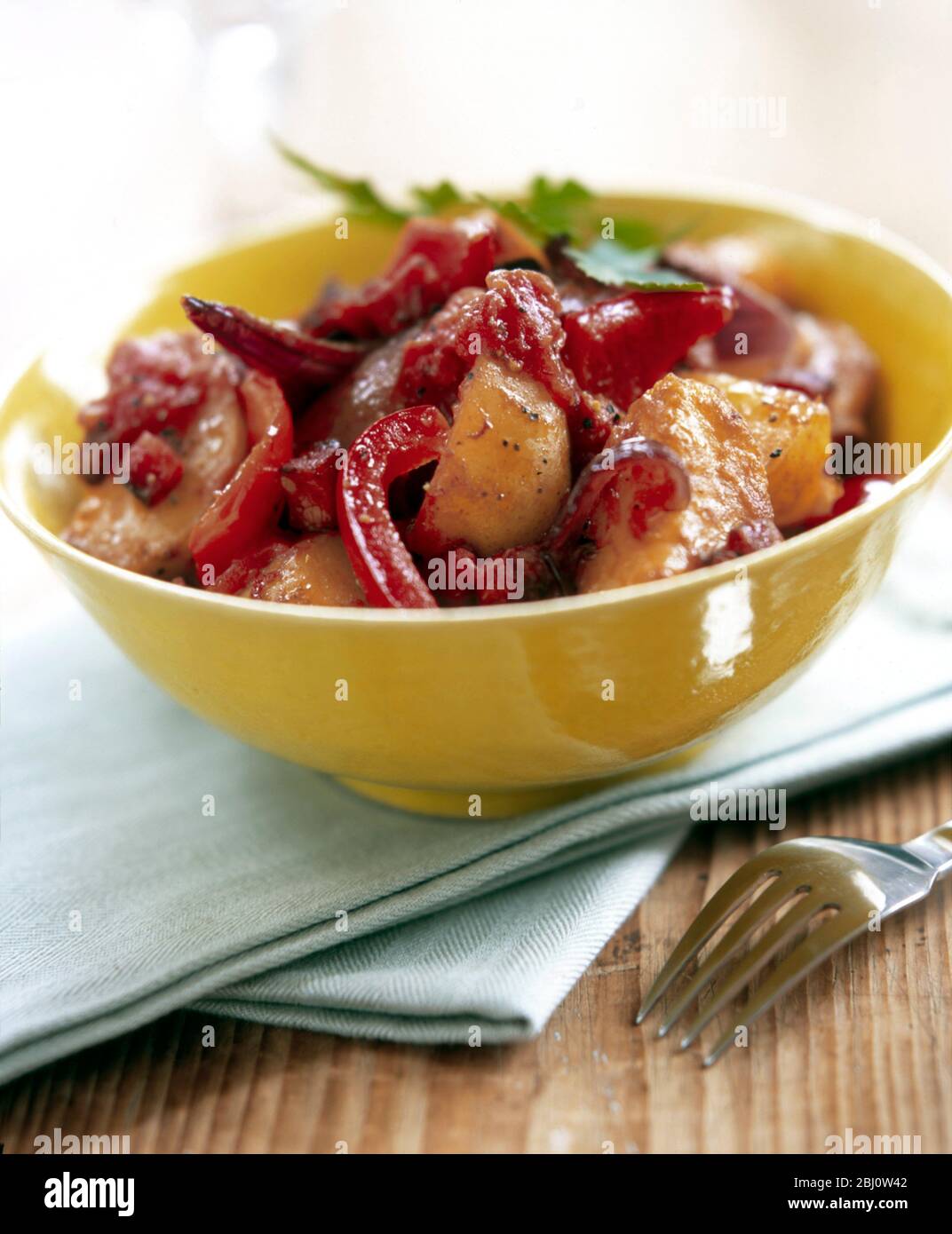 Yellow bowl of potatoes roasted with strips of red pepper and red onions with mustard dressing - Stock Photo
