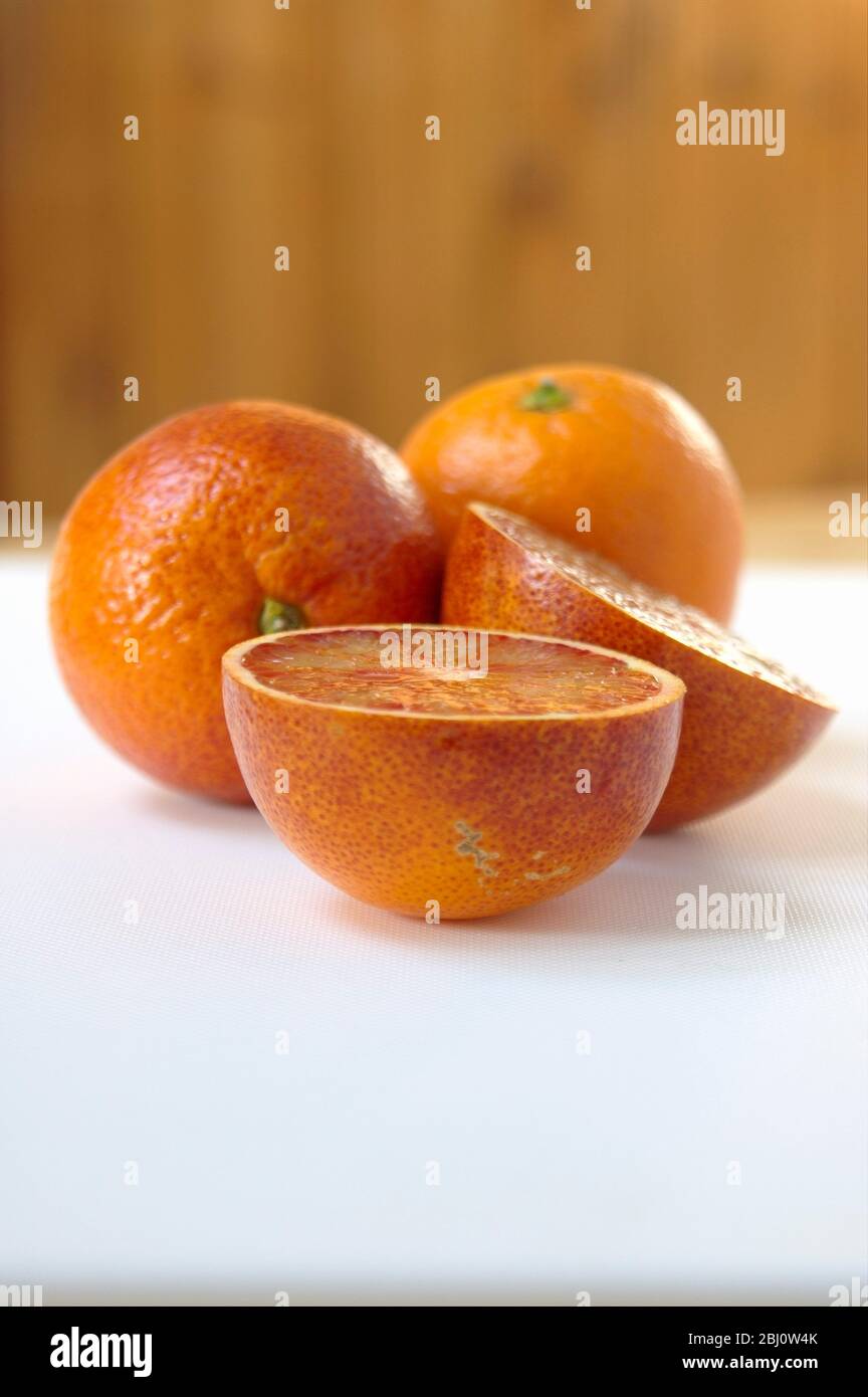 Oranges, cut and whole on white surface with wooden b ackground - Stock Photo