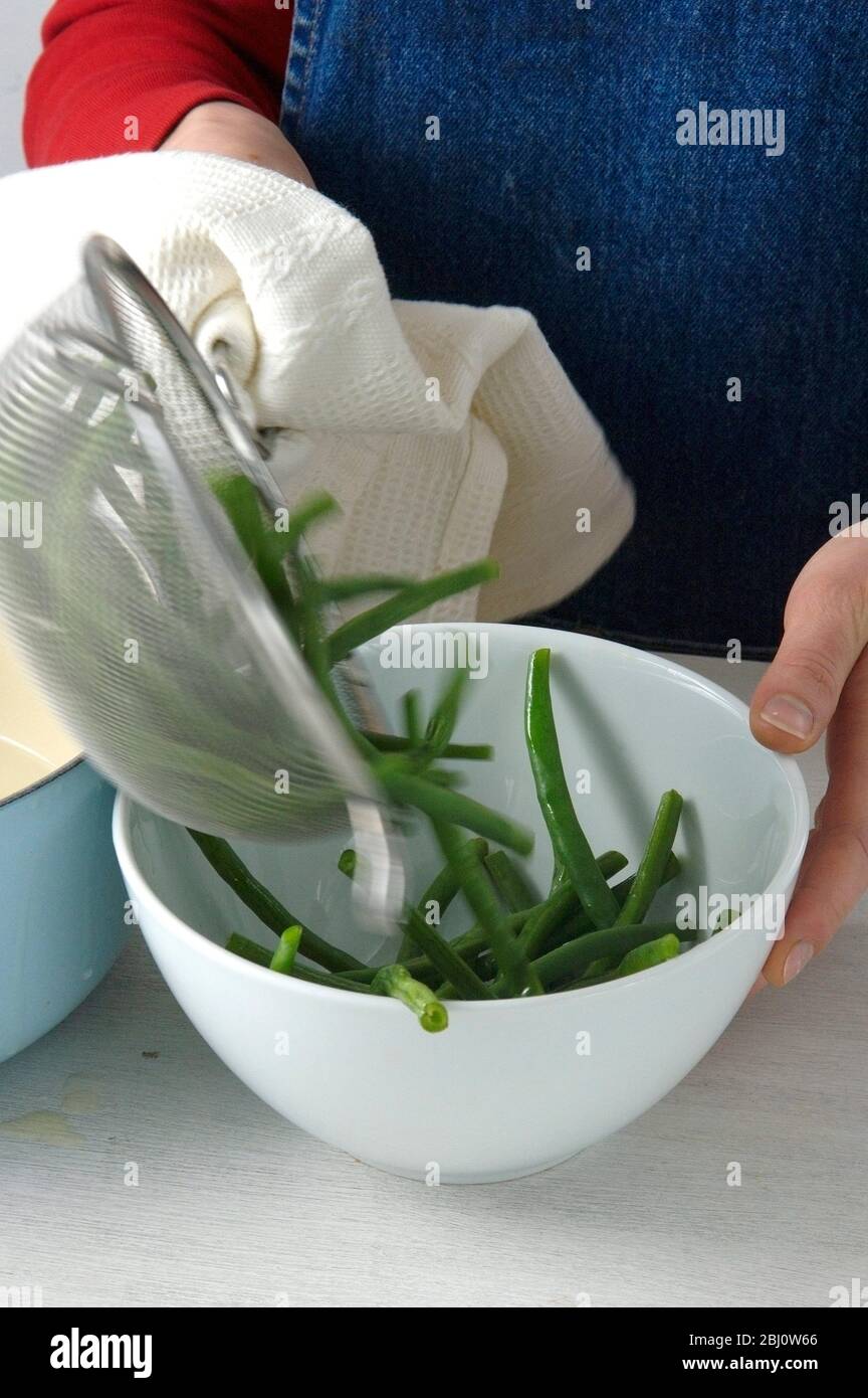 Turning green french beans out of a sieve after having drained them - Stock Photo