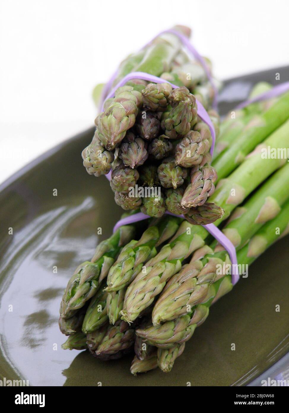Two bunches of asparagus on green plate - Stock Photo