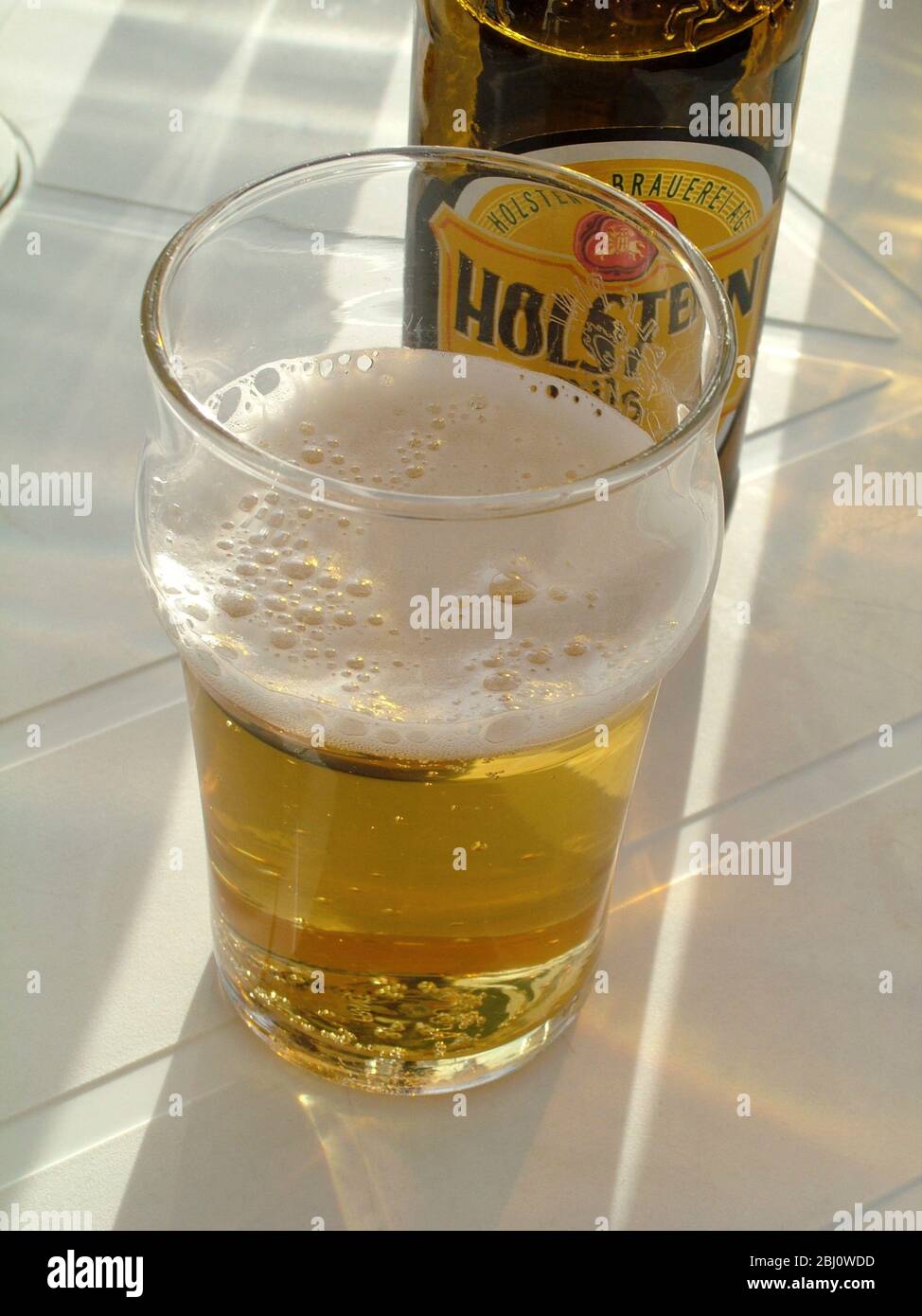 Glass half full of lager in sunshine at seaside cafe - Stock Photo