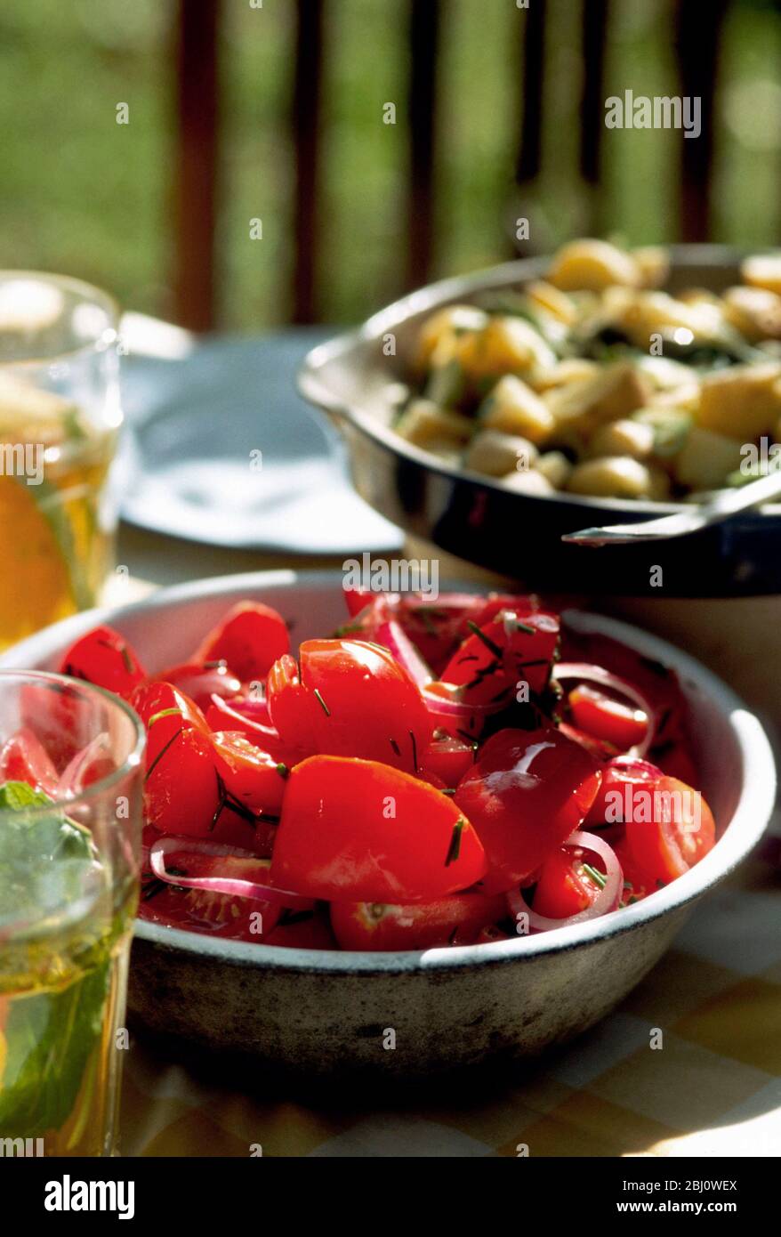 Old metal bowl of tomato salad with soft focus potato salad behind - Stock Photo