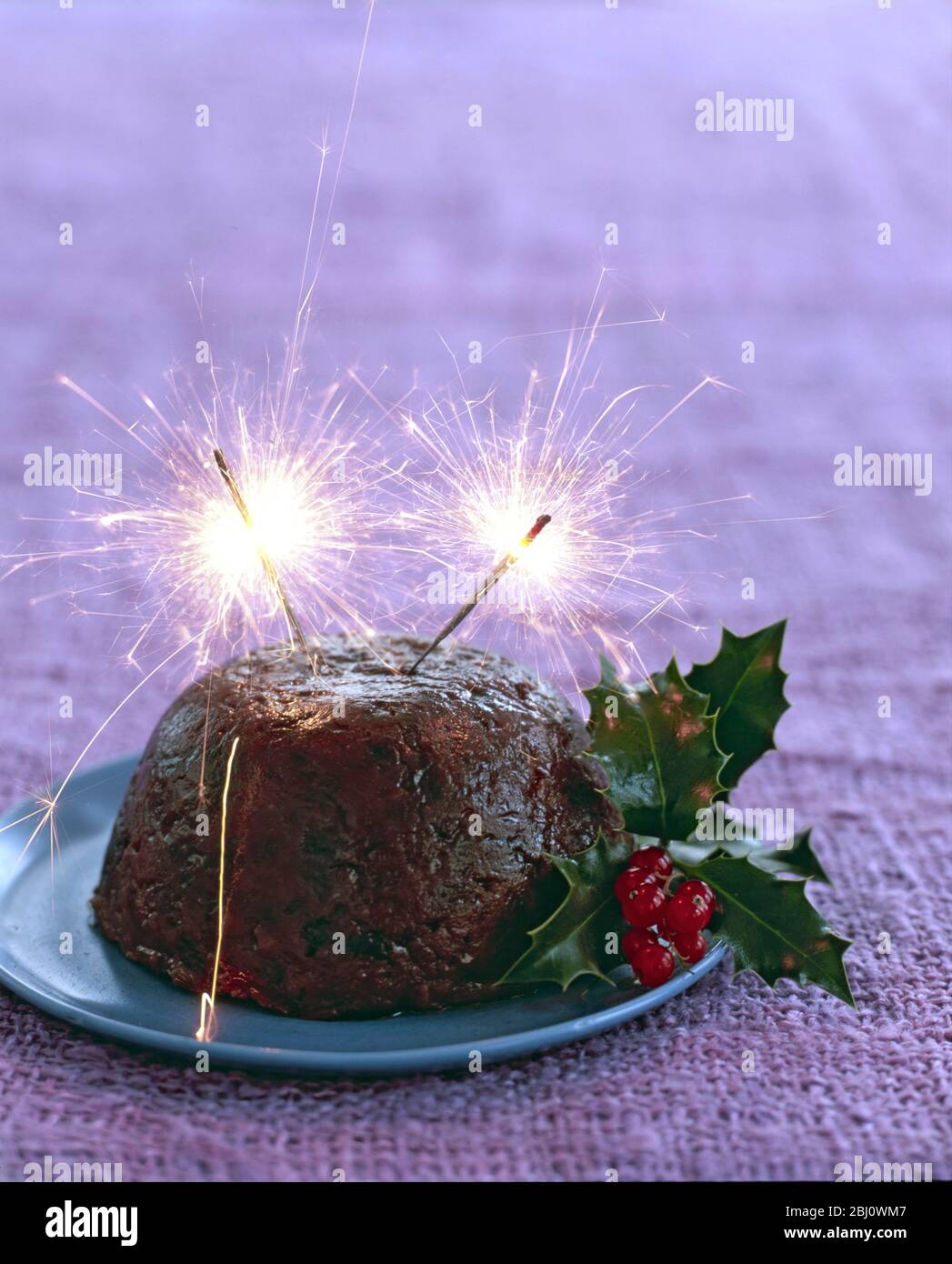 Traditional British Christmas pudding with with holly and berries and sparklers alight on top - Stock Photo