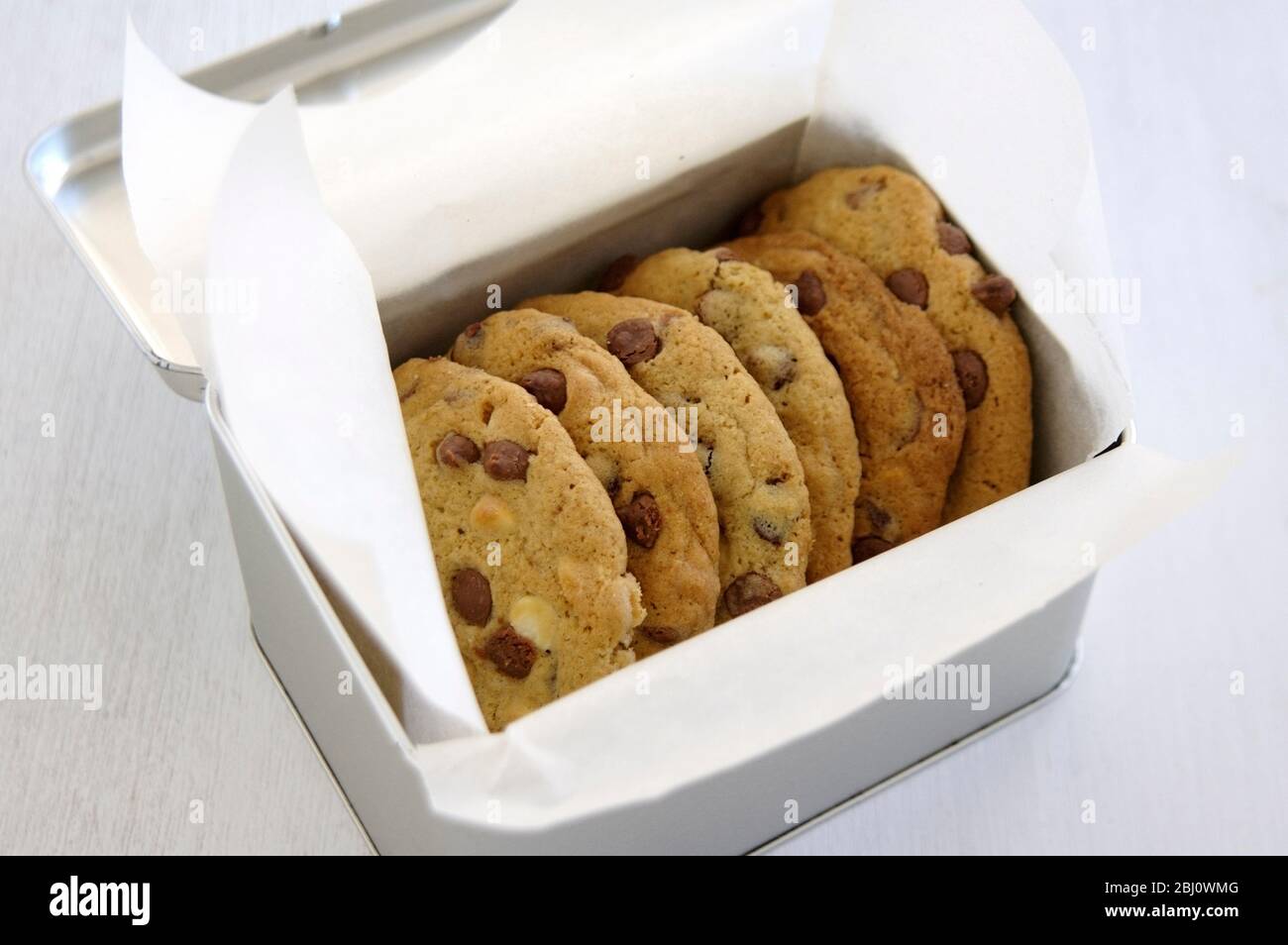Metal tin of chocolate chip cookies wrapped in white greaseproof paper - Stock Photo