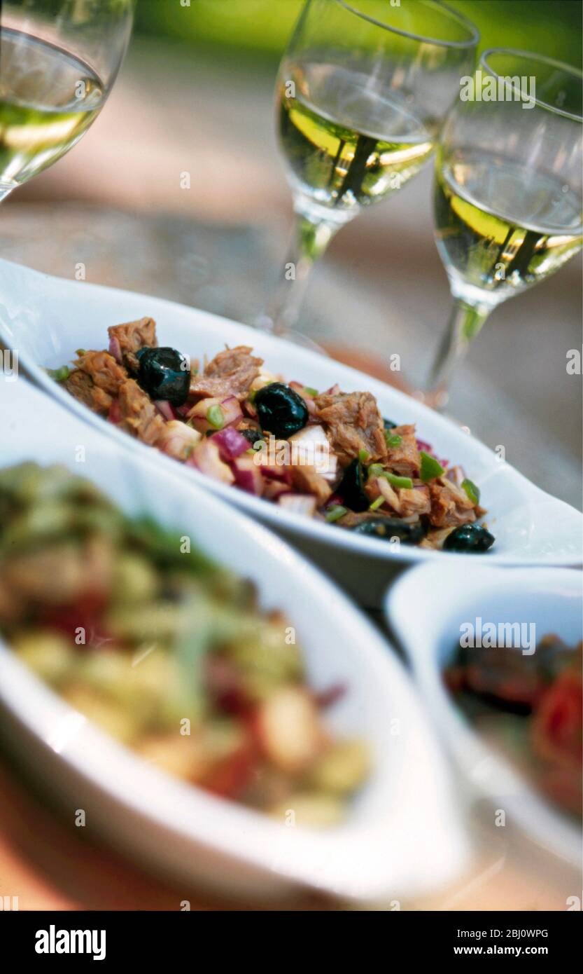 Summer tapas style meal outdoors in French garden with small dishes of various salads in including tuna with black olives, red onion and herbs with gl Stock Photo