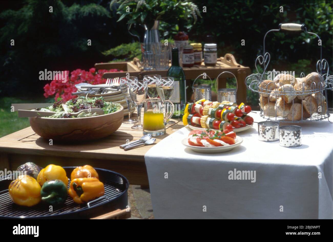 Smart barbecue lunch table outside in sunshine, salad in large wooden bowl, tomato and mozzarella salad, vegetable kebabs, olive oil dressing, bread r Stock Photo