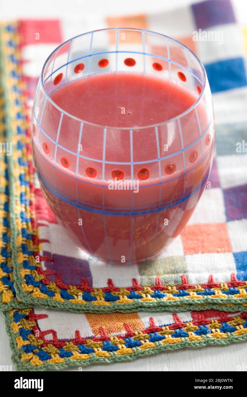Decorative painted glass of red raspberry smoothie on bright checked napkin - Stock Photo