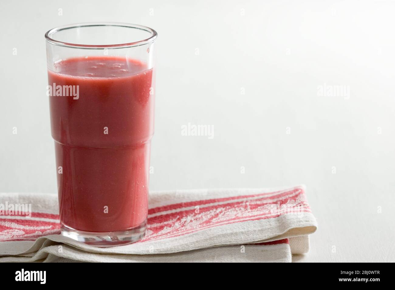 Glass of red raspberry smoothie on vintage red and cream cloth - Stock Photo