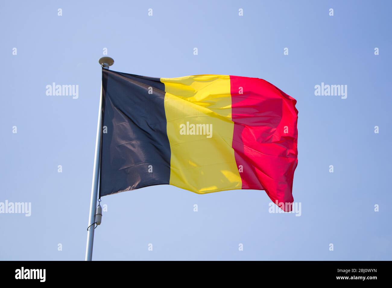 The flag of belgium waving on the wind behind a blue background Stock Photo