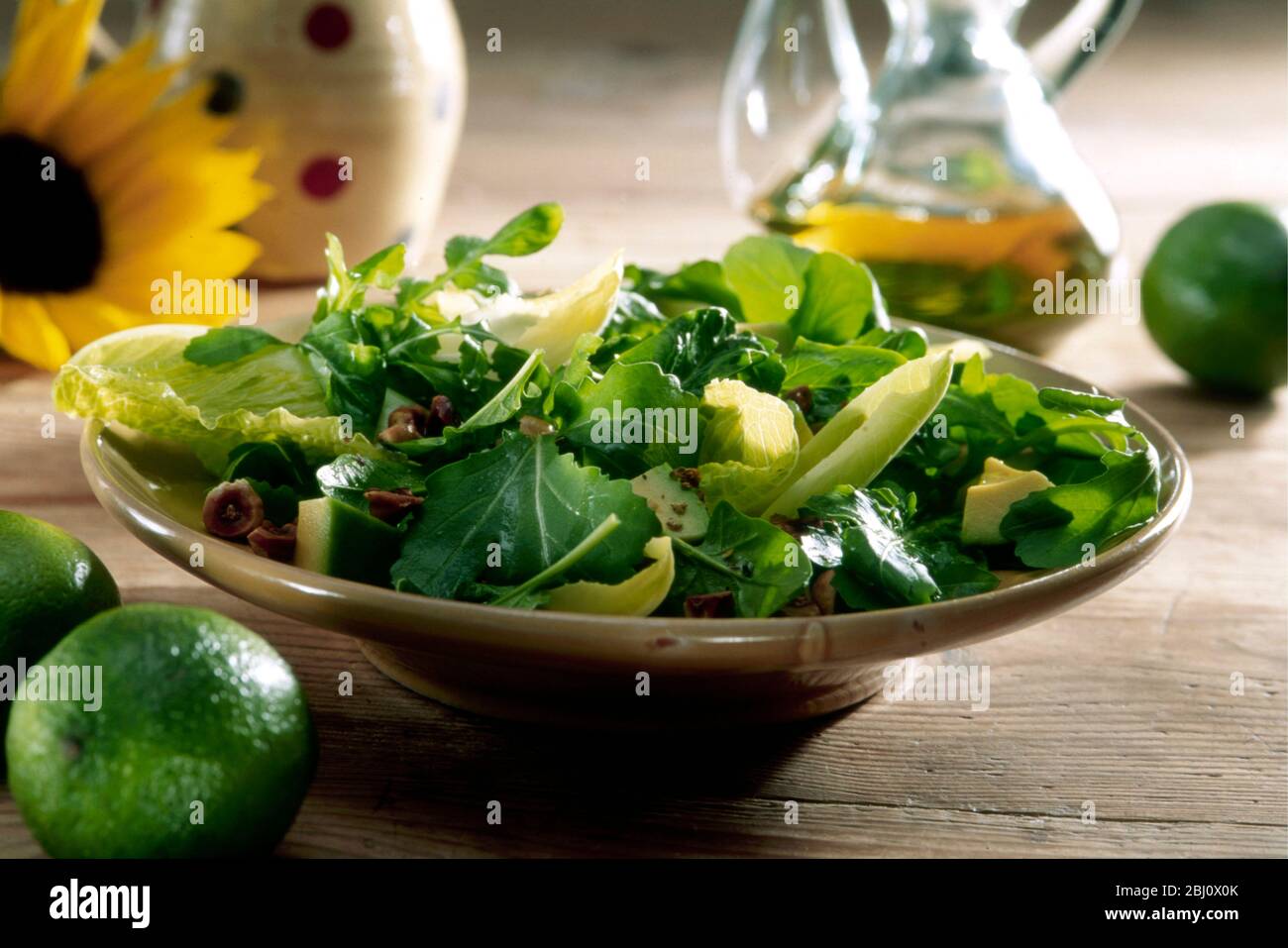 MIxed salad of various leaves including watercress, lambs lettuce, romaine, with avocado and chopped walnuts and hazelnuts with dressing in bottle of Stock Photo