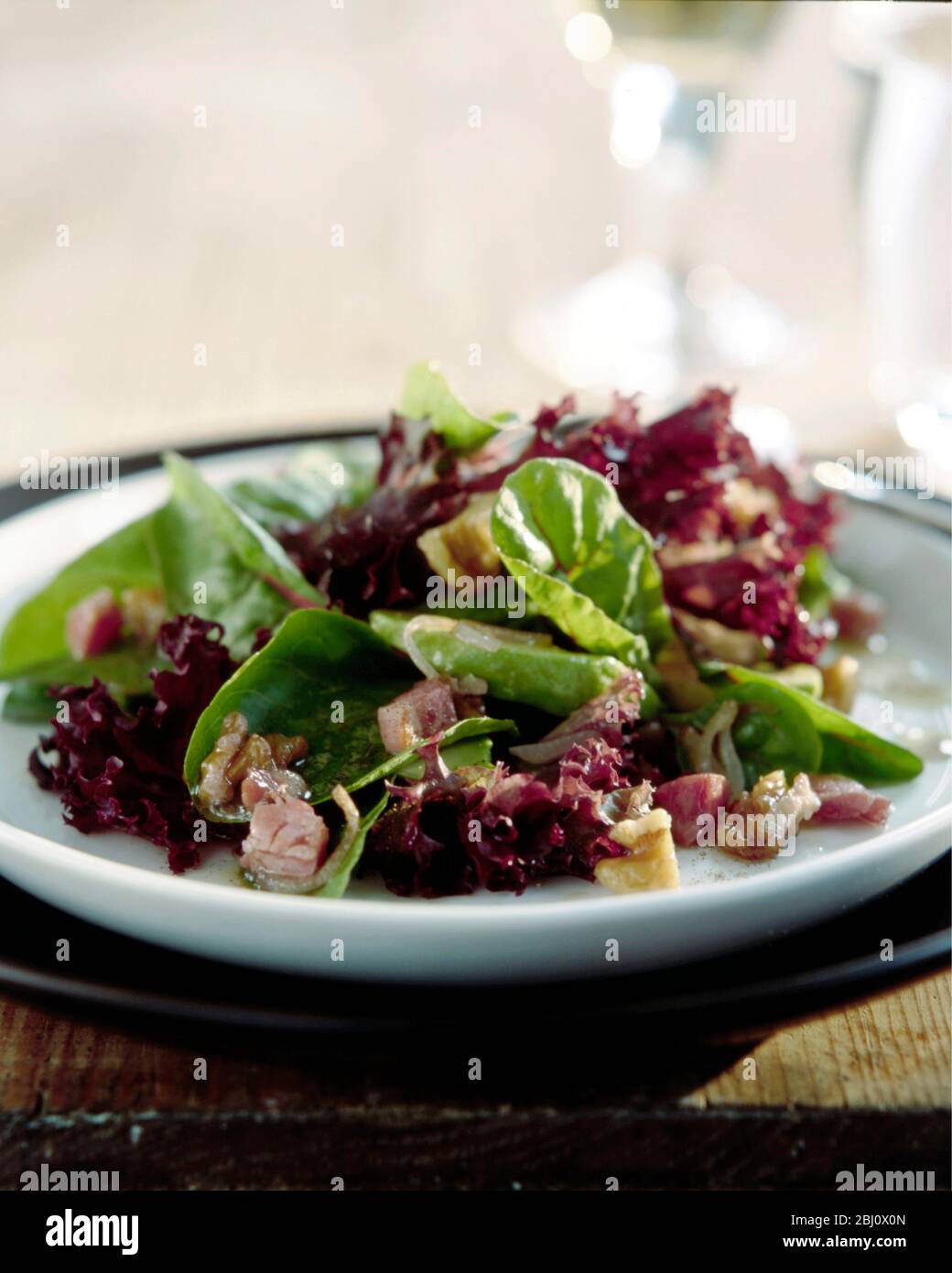 MIxed salad of various leaves including lollo rosso, lambs lettuce, radicchio, with lardons and chopped walnuts and hazelnuts with dressing on rustic Stock Photo