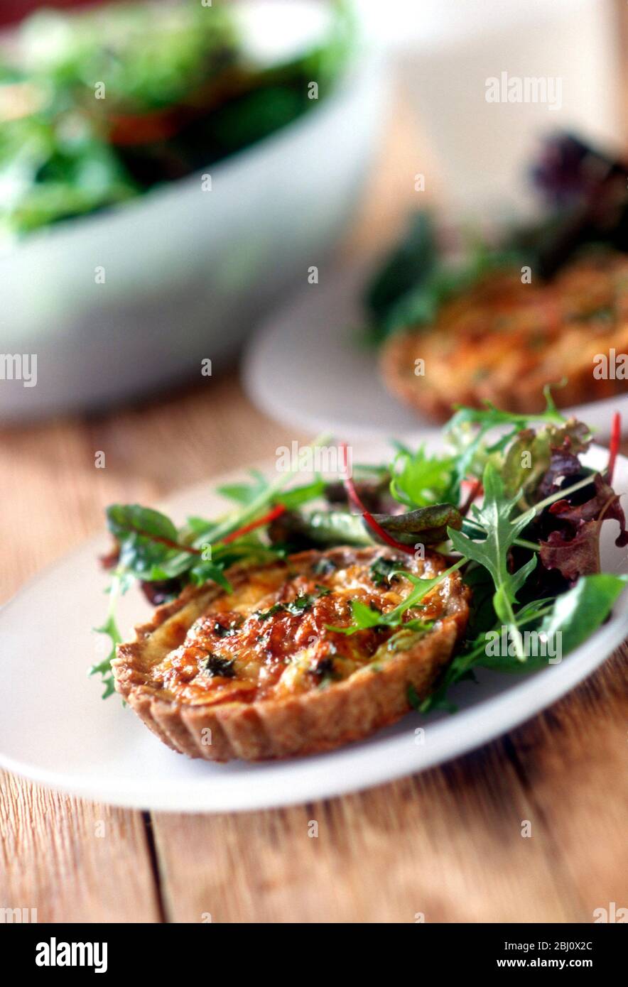Tomato and cheese quiche served with mixed leaf salad on white plate - Stock Photo