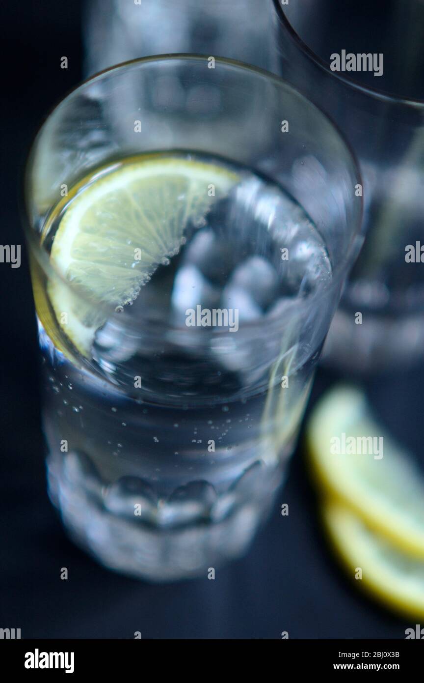 Glass of lightly sparkling Pellegrino, Italian mineral water, wirh small wedge of lemon on dark tray - Stock Photo