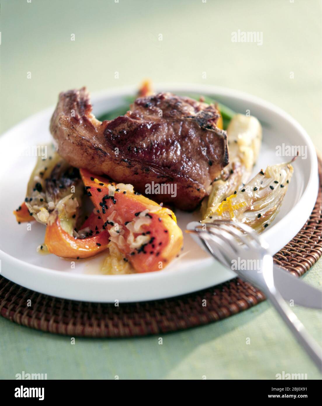 Grilled lamb cutlet on roast vegetables, on white plate, with roast squash fennel and sesame seeds - Stock Photo