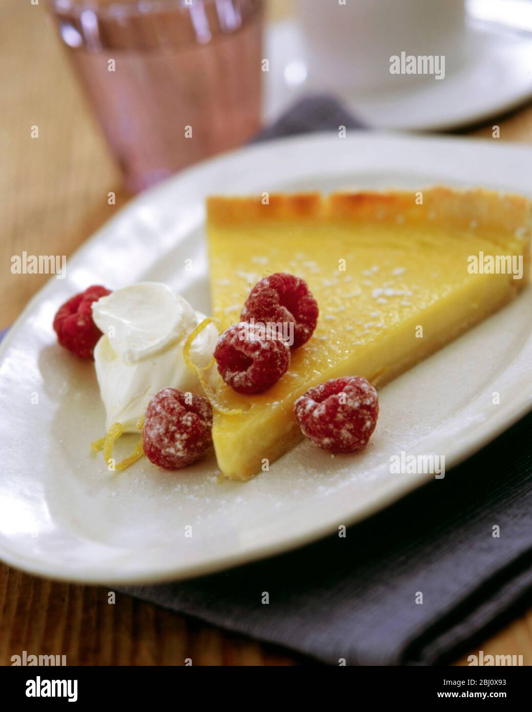 Slice of classic lemon tart served with fresh raspberries, lemon zest and creme fraiche - Stock Photo