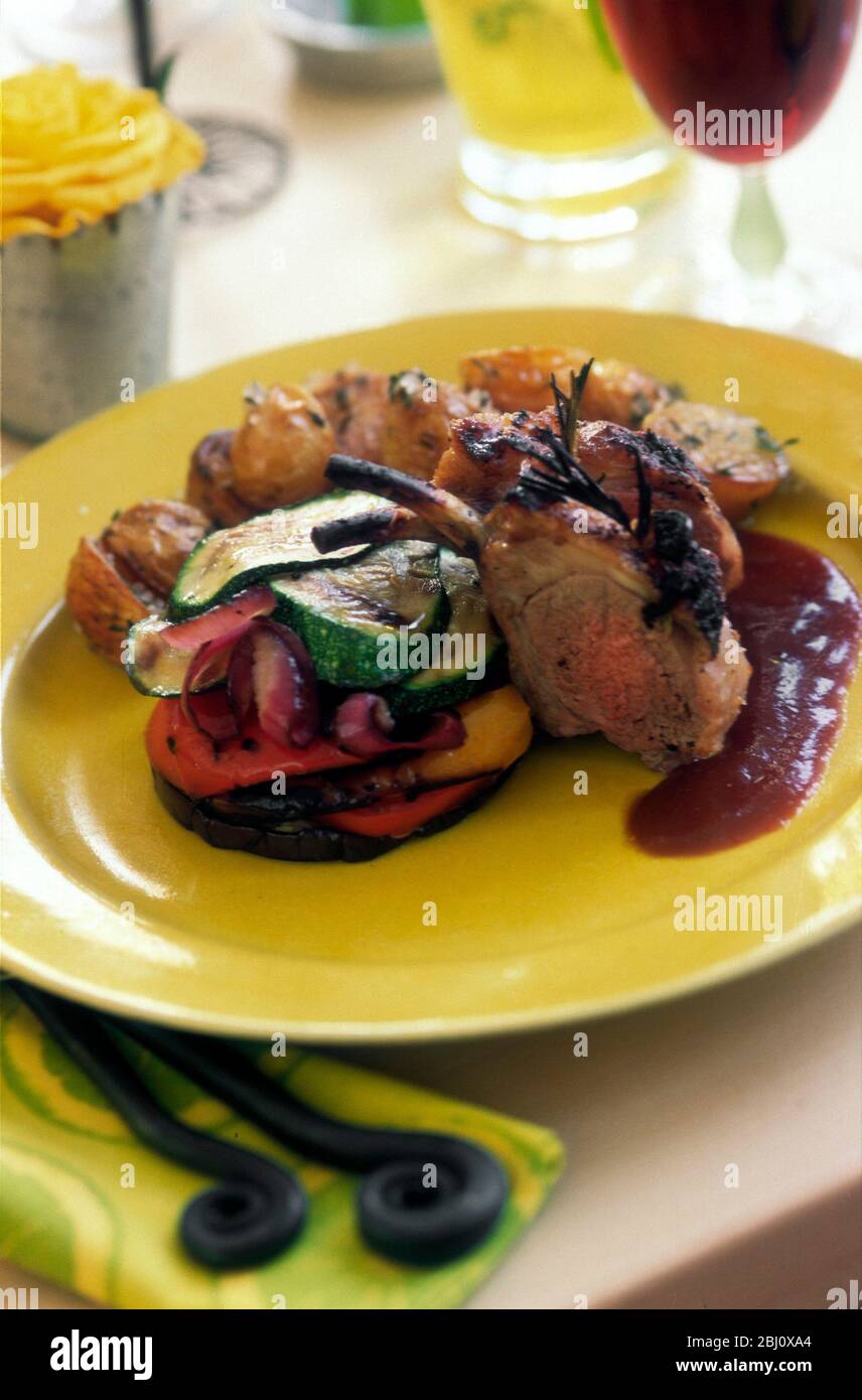 Roast lamb on mixed roast vegetables with gravy on yellow plate in lunch party setting - Stock Photo