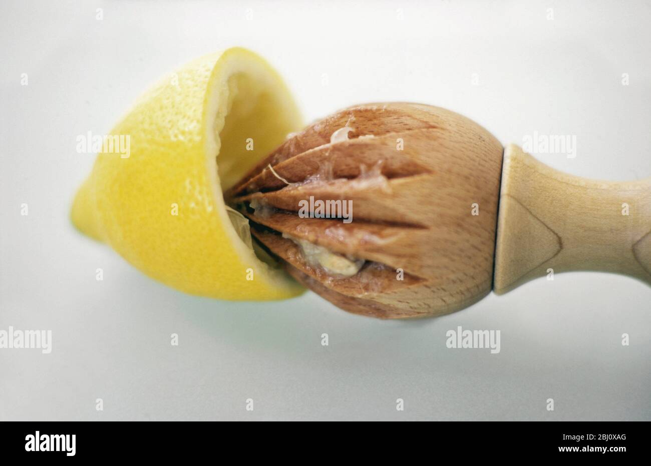 Classic wooden lemon squeezer being used to extract juice from lemon half - Stock Photo