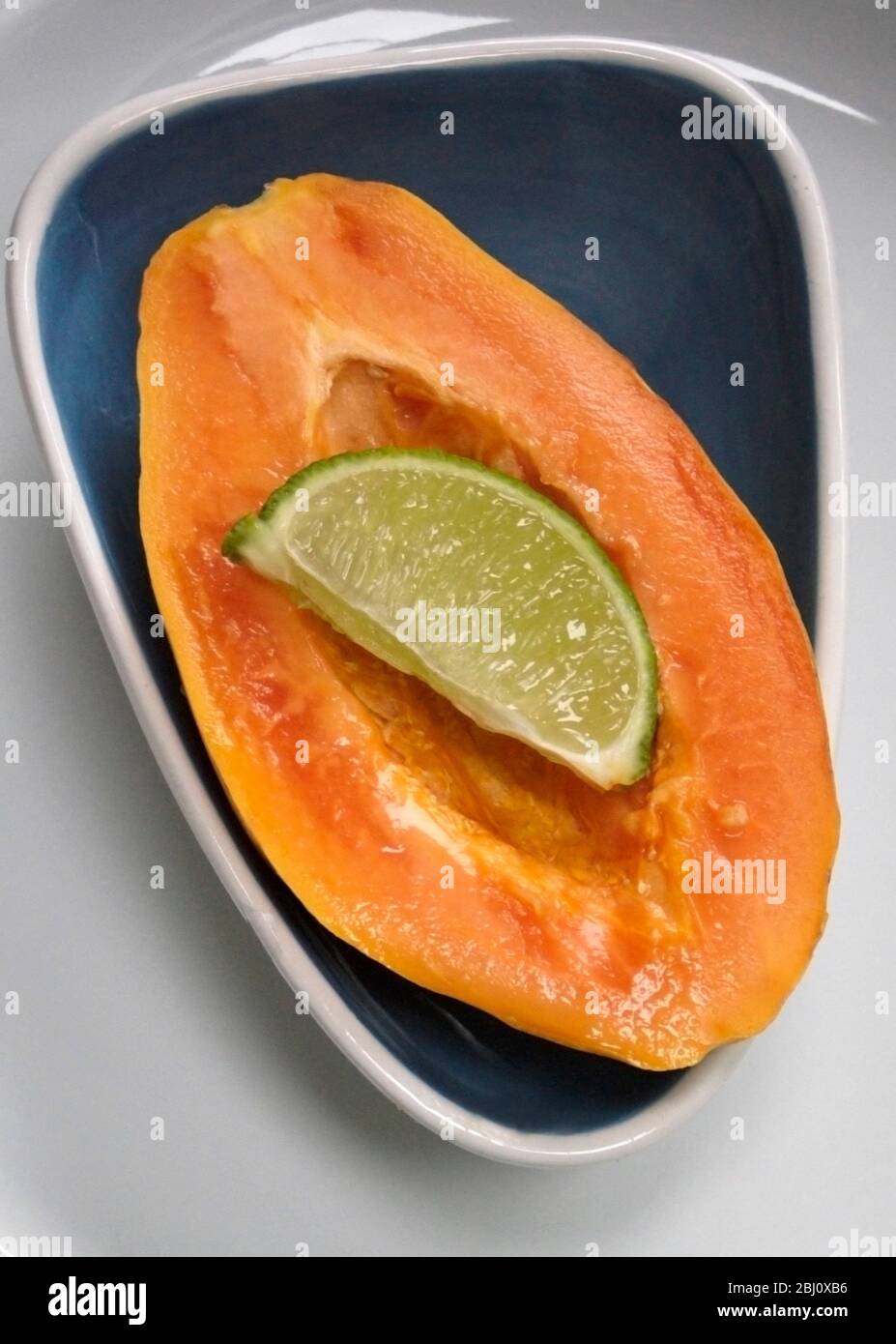 Halved papaya in modern blue dish with wedge of lime ready to be squeezed on - Stock Photo