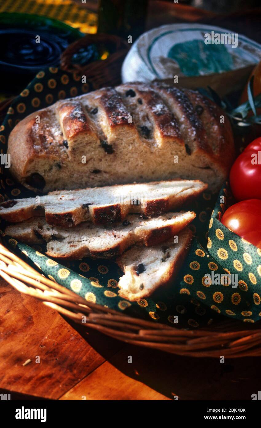 French olive bread with tomatoes and cheese in basket in gentle warmth of spring sunshine - Stock Photo