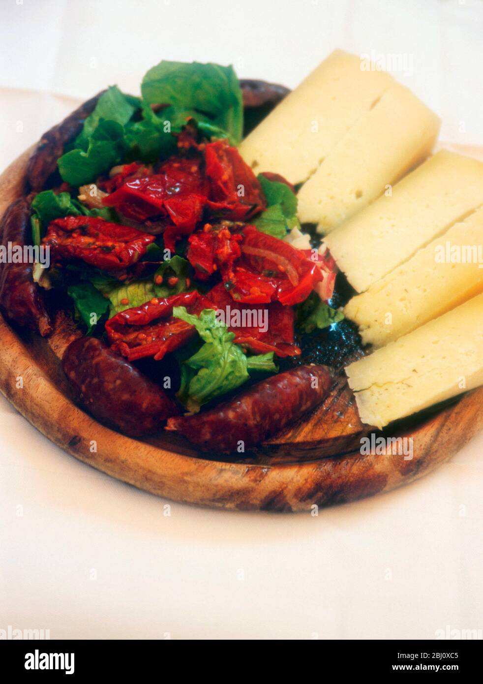 Wooden platter of pecorino cheese with Italian sausages and salad of lettuce with roasted peppers - Stock Photo