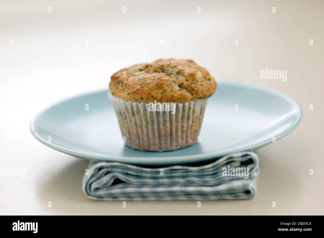 Single poppyseed muffin on blue plate on check napkin, on painted table. - Stock Photo