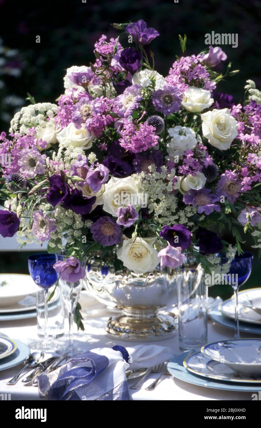Amazing blue and white flower arrangement in the middle of formal table setting arranged outside in summer garden - Stock Photo
